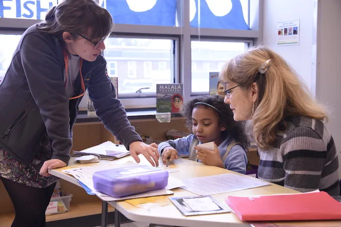 an americorps member pointing at a part of a lesson that a tutor and student are working on