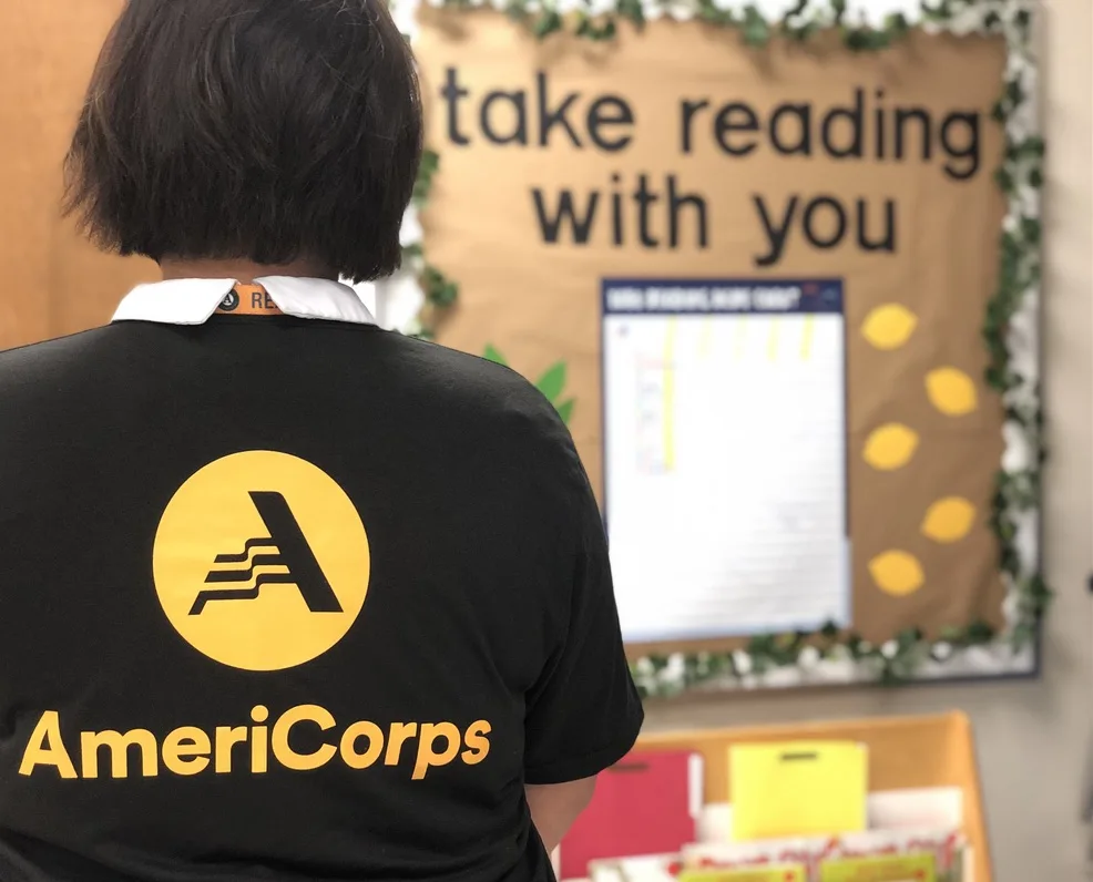 an americorps member facing away from the camera, but their black shirt has a large, yellow americorps logo on the back