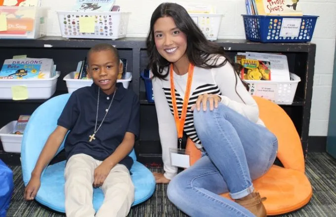 volunteer tutor and student sitting on the floor and smiling at the camera