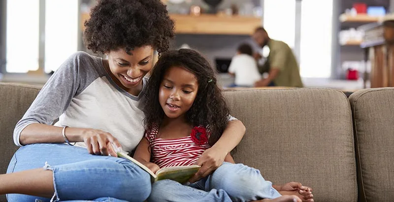 a parent and student read together on a couch, enjoying the free tutoring in Newark that Reading Partners offers