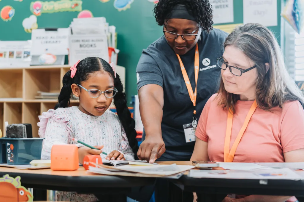 inclusive literacy; an americorps member pointing at literacy resources in between a student and her tutor