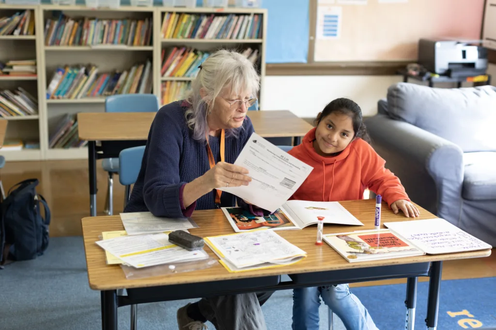 a student and tutor during a tutoring session, the student smiling at the camera while the tutor holds up a worksheet