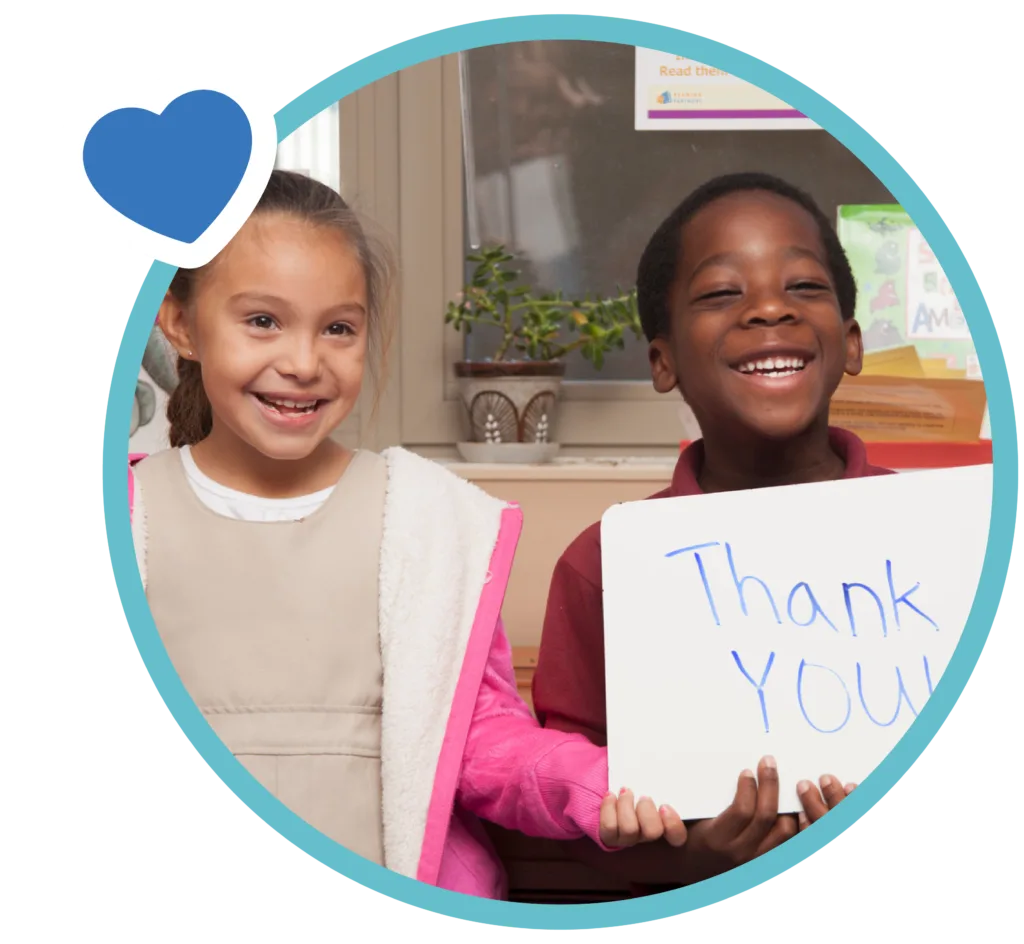 two students smiling at the camera, one of them holding a whiteboard that reads "Thank you!"