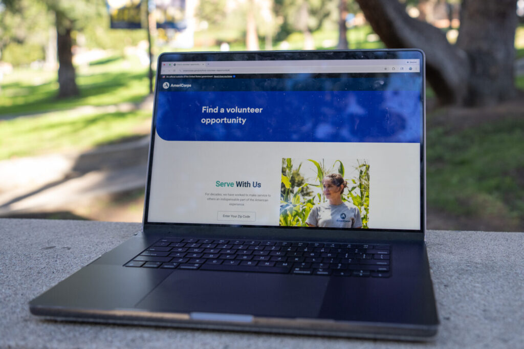 The AmeriCorps volunteer website is pictured on a computer on a table outside. Federal funding cuts have left the futures of thousands of volunteering opportunities for California college students uncertain since April 2025. (Joice Ngo/Daily Bruin)