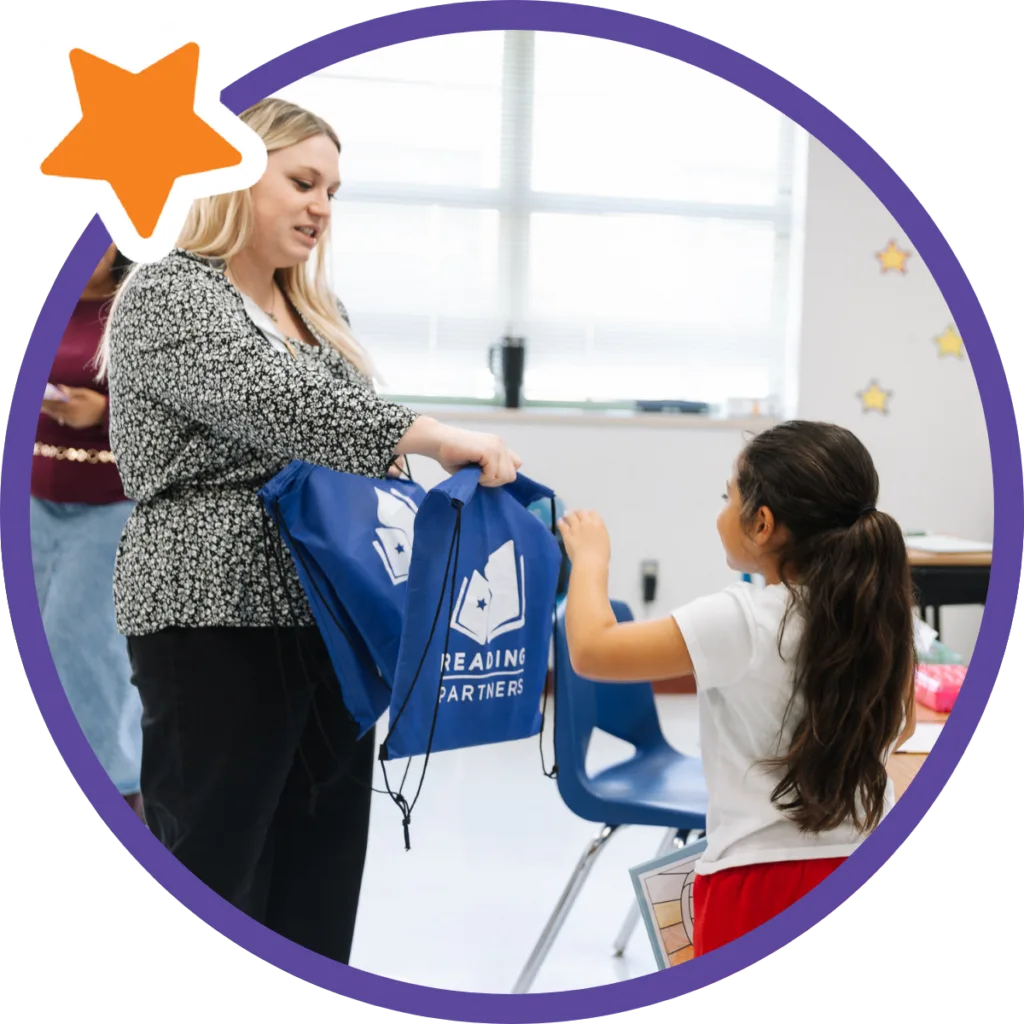 reading partners staff member handing a student a bag full of books